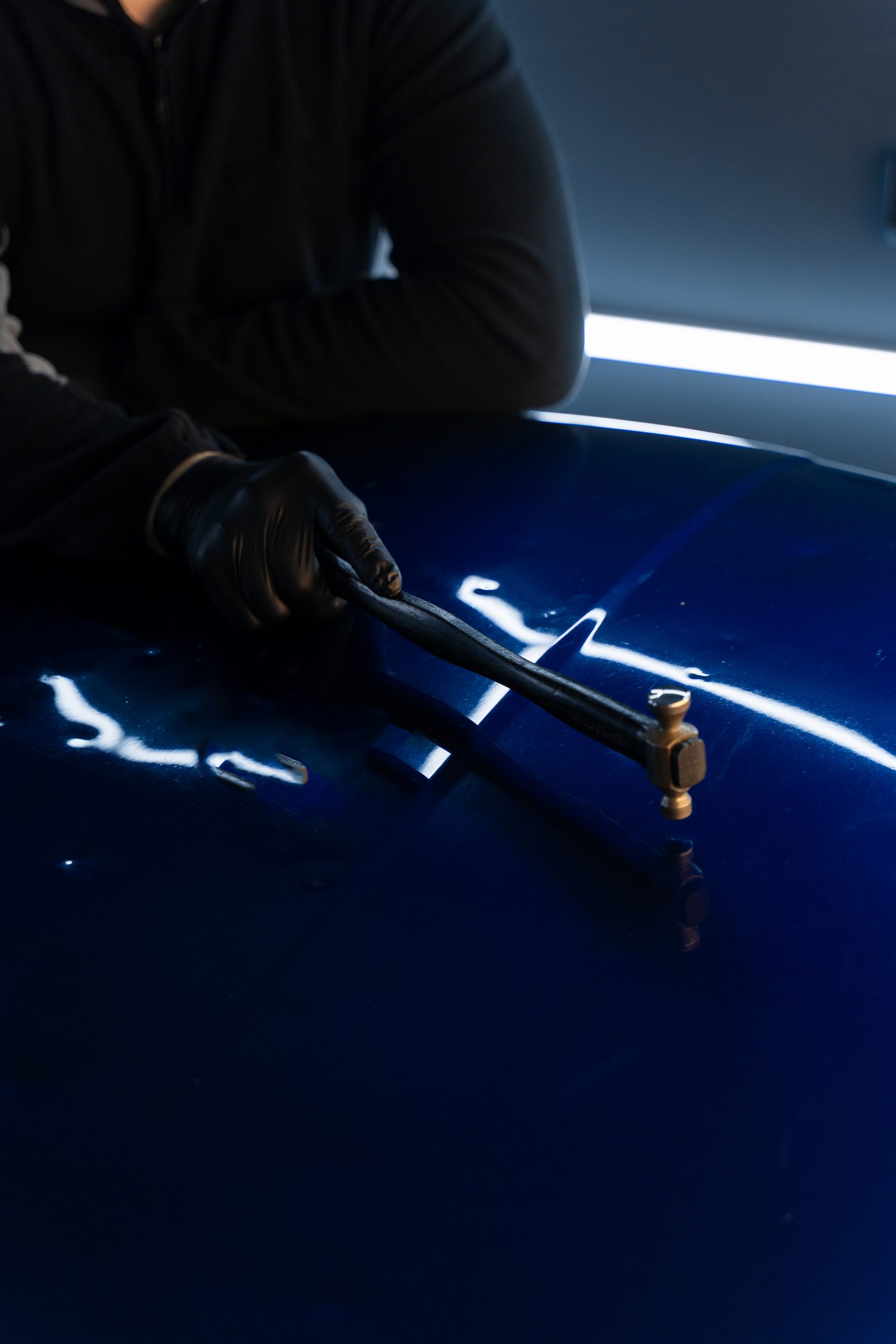 Technician working a moody dark-blue panel with a body hammer