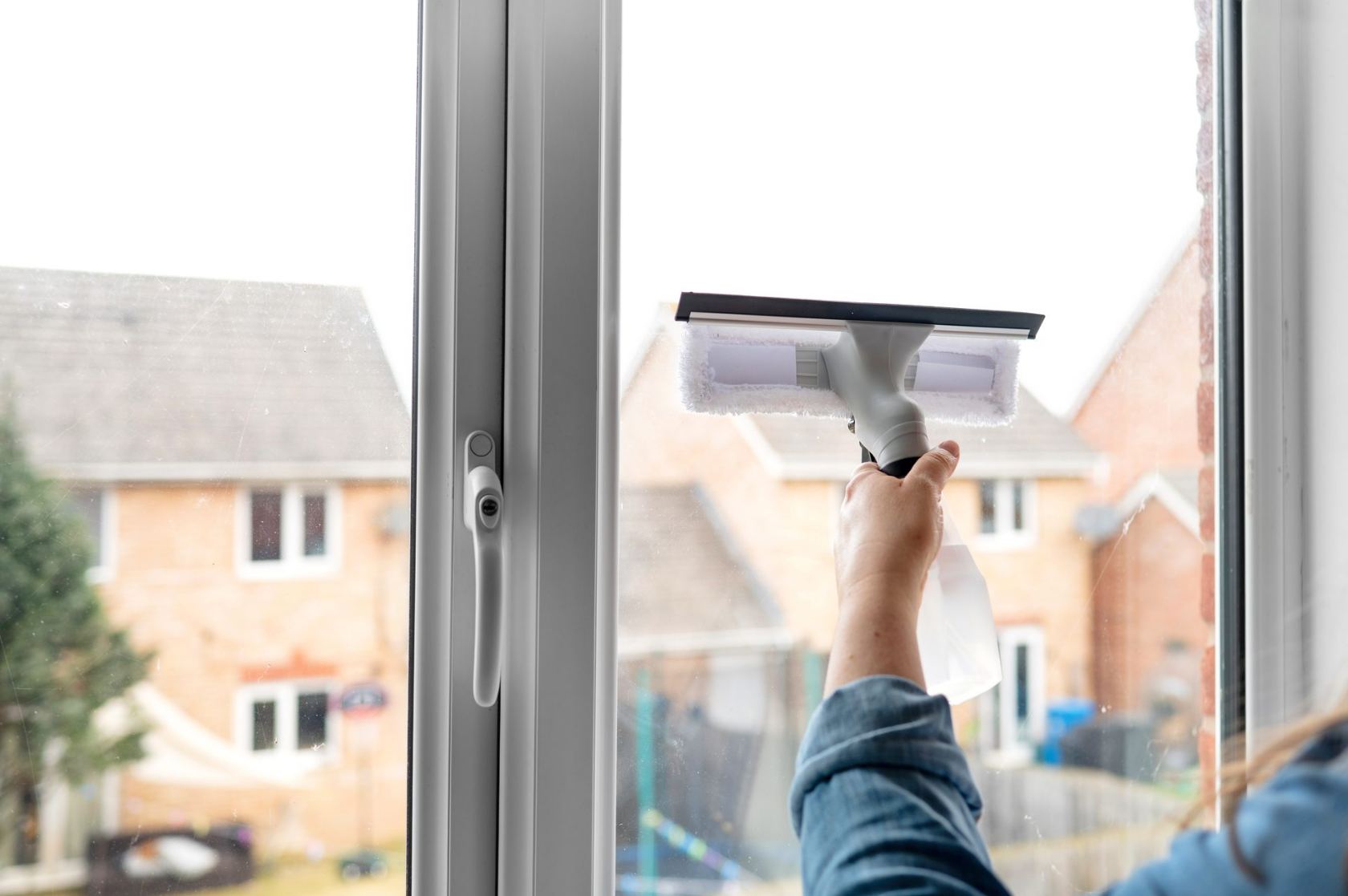 Squeegee gliding down a home window from inside, the neighborhood beyond the glass